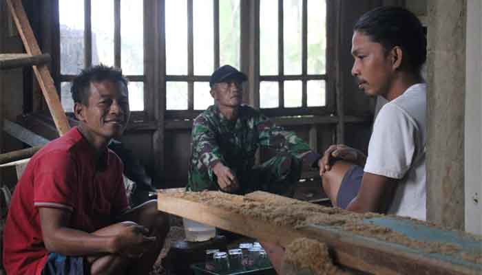 Agus duduk bersama warga lain dan Satgas TMMD Reguler ke-128 Kodim 0702/Purbalingga dengan dinding rumah baru